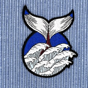 May include: Embroidered patch featuring a white whale tail with black outlines, emerging from blue water with white waves. The patch is perfect for adding a nautical touch to clothing, bags, or other accessories.