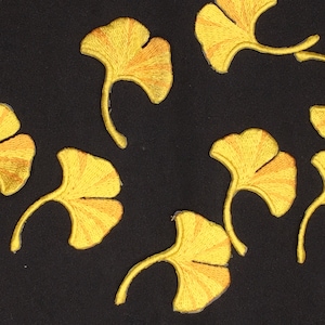 May include: A black fabric background with nine yellow embroidered ginkgo leaves. The leaves are arranged in a random pattern.