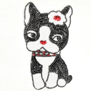 May include: A sequined illustration of a Boston Terrier dog. The dog is black and white with a red nose and collar. A white flower with a red center adorns its head. The dog is sitting upright.