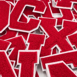 May include: A pile of red felt letter patches with white outlines. The letters are in various sizes and are all uppercase.