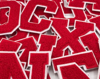 May include: A pile of red felt letter patches with white outlines. The letters are in various sizes and are all uppercase.