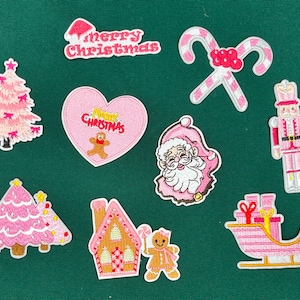 May include: Pink felt Christmas ornaments with various designs, including a Christmas tree, a gingerbread house, a candy cane, a Santa Claus, a nutcracker, and a sleigh. The ornaments feature embroidered details and the text "Merry Christmas".