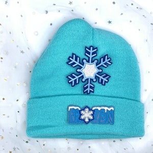 May include: A light blue knit beanie with a white snowflake and "FROZEN" embroidered on the front.