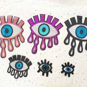 May include: Six colorful eye-shaped patches with sequins and eyelashes. The eyes are blue, with white and black accents. The patches are pink, purple, and black.
