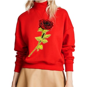 May include: Red sweatshirt with a gold and red rose embroidered on the front.