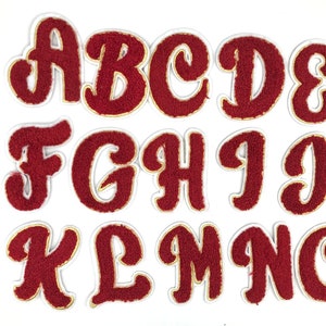 May include: A set of 14 red felt letters with gold outlines, in a cursive font, representing the alphabet from A to N.