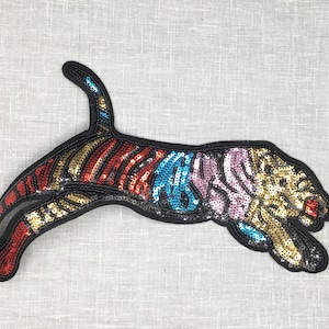 May include: A colorful sequined tiger applique patch. The tiger is leaping and has a gold, red, blue, and pink color scheme.