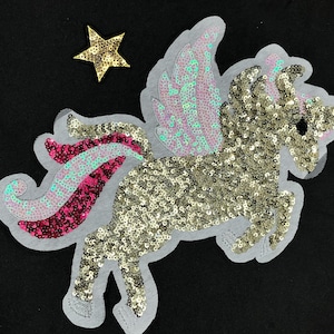 May include: A gold sequined unicorn with pink and blue wings and a pink and blue tail. The unicorn is on a white background with a gold star.