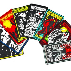 May include: A set of nine embroidered patches featuring various cryptids, including the Mothman, Jersey Devil, Sasquatch, Flatwoods Monster, and Chupacabra. Each patch features a black background with white and yellow outlines, and the text "Cryptozoology Tracking Society" is printed on each patch.