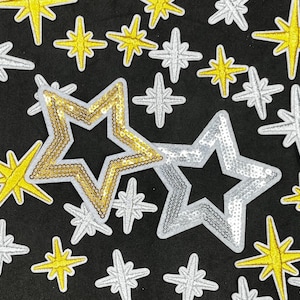 May include: A collection of star-shaped patches in various sizes and designs. Some stars are silver, others gold, and some are yellow. The patches are embellished with sequins and embroidery, set against a black background.