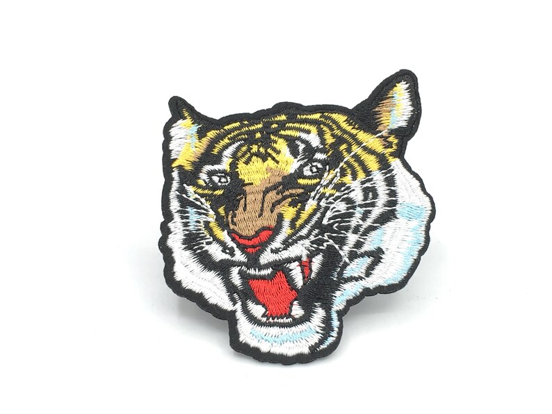 May include: Embroidered iron-on patch featuring a tiger's face with a fierce expression. The tiger has black, white, and yellow stripes and a red open mouth.