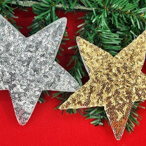 May include: Two sparkly star-shaped ornaments, one silver and one gold, on a red background. The stars are made of sequins and are perfect for adding a festive touch to any holiday decor.