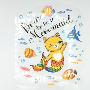 May include: A yellow cat with a rainbow tail is dressed as a mermaid. The text "Born to be a Meowmaid" is written in black on a white background. The image is surrounded by colorful fish.