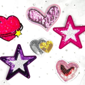 May include: A collection of sequined patches in various shapes, including hearts and stars. The patches feature vibrant colors like pink, purple, and gold, with white sequin accents. Some have black outlines and yellow star details.