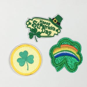 May include: Three embroidered iron-on patches with a St. Patrick's Day theme. One patch features a shamrock and the text "Happy St. Patrick's Day". Another patch features a shamrock with a rainbow. The third patch features a shamrock with a yellow background.