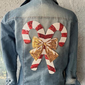 May include: A blue denim shirt with a red and white candy cane and gold bow applique on the back.