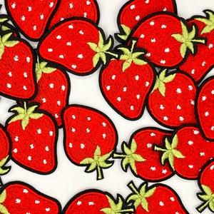 May include: A collection of red and white embroidered strawberry patches. The strawberries are various sizes and have a detailed design with white stitching.
