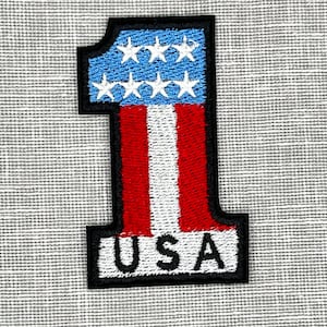 May include: A red, white, and blue embroidered patch shaped like the number one with the word "USA" underneath.