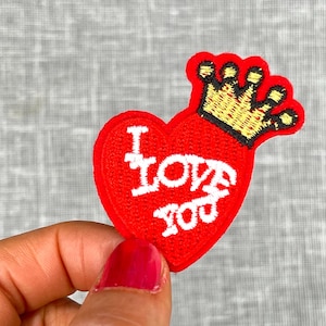 May include: Red felt heart-shaped patch with a gold crown on top. The heart has white embroidery that says "I LOVE YOU".