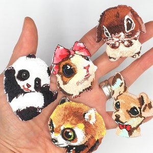 May include: Five embroidered iron-on patches featuring cute cartoon animals. The patches include a panda, a guinea pig wearing a red bow, a brown rabbit, a red panda, and a chihuahua.