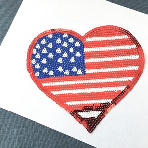 May include: A red, white, and blue heart-shaped American flag made of sequins.