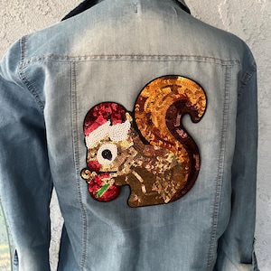 May include: A light blue denim jacket with a sequined squirrel wearing a Santa hat and holding a red candy cane on the back.