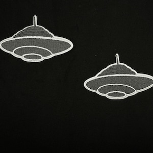 May include: Two white embroidered iron-on patches of flying saucers on a black background.