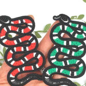 May include: Two embroidered iron-on patches of snakes. One snake is red and black, the other is green and black.