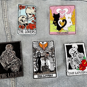 May include: Five iron-on patches featuring the tarot card "The Lovers". Each patch has a different design, including skeletons, cats, and a couple standing under a crescent moon. The patches are all black and white with pops of color.