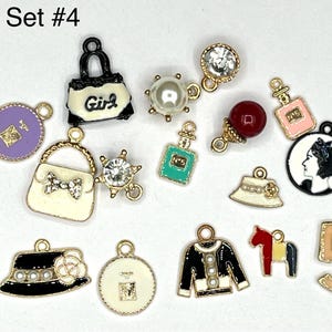 May include: Set of 14 gold-tone charms with various designs, including a purse, perfume bottles, a hat, a number 5, a horse, and a Chanel-inspired jacket. The charms are on a white background.