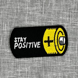May include: Black and yellow embroidered patch shaped like a battery with the text "STAY POSITIVE" in white.