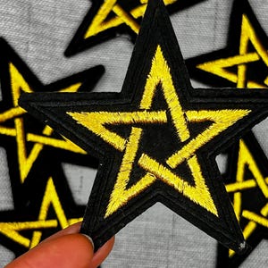 May include: Black and yellow embroidered star patches. The patches feature a black border with a yellow, five-pointed star design in the center. The star design is made with yellow thread. The patches are likely for clothing or accessories.