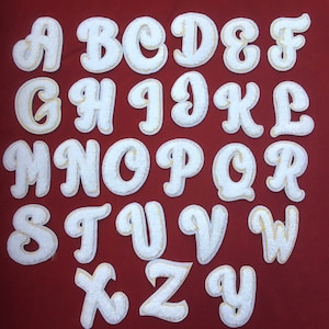 May include: White felt letters of the alphabet in a cursive font with a gold outline. The letters are arranged in alphabetical order.