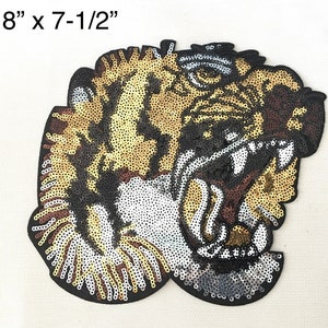 May include: A large, detailed, embroidered iron-on patch of a tiger's face with a fierce expression. The tiger is made of gold, silver, and black sequins. The patch measures 8 inches by 7-1/2 inches.