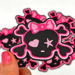 May include: Pink and black embroidered skull patch with a pink bow and a pink heart and star on the skull.