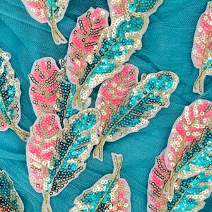 May include: A collection of teal, pink, and gold sequined feather patches. The patches are arranged on a teal mesh fabric.