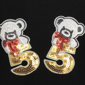 May include: Two gold sequined patches with a white bear wearing a red bow on top of the number 5.