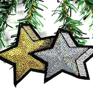 May include: Two star-shaped patches with black borders. One patch is gold with sequins, and the other is silver with sequins. Green garland is in the background.