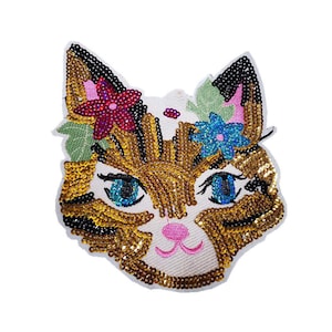 May include: A colorful embroidered cat face patch with gold, black, and brown sequins. The cat has blue eyes and a pink nose. The cat is wearing a flower crown with pink, blue, and green flowers.