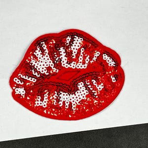 May include: Red sequin lips patch. This iron-on patch features a red lip design with white sequins.