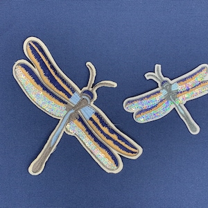 May include: Two embroidered dragonfly patches with iridescent sequins on a dark blue background. The larger dragonfly is brown and blue with a light blue body. The smaller dragonfly is brown and light blue with a light blue body.