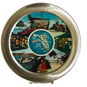 May include: A silver metal tray with a round, colourful design featuring images of Florida, including azaleas, flamingos, fishing, bathing, and a map of the state. The text "Florida" is printed in the centre of the tray.