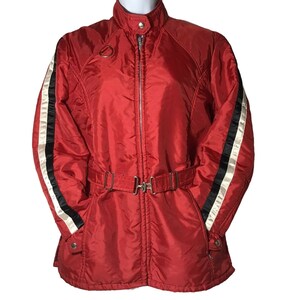 May include: Red ski jacket with black and white stripes on the sleeves and a belt. The jacket has a zipper closure and a stand-up collar.