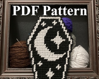 Puede incluir: Un patrón de punto de cruz en blanco y negro de un ataúd con una luna creciente y estrellas. El patrón está enmarcado en un marco marrón oscuro con el texto "PDF Pattern" arriba.