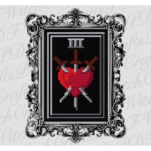 May include: A framed cross-stitch design featuring a red heart pierced by three swords. The design is set against a black background with the Roman numeral III at the top. The frame is ornate, with a black and white floral pattern.