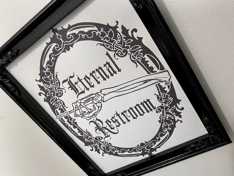 May include: A black framed print with a white background. The print features a skeletal hand pointing to the right with the text "Eternal Restroom" in a gothic font.