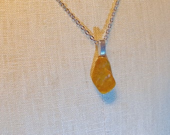 May include: A silver chain necklace with a yellow gemstone pendant. The pendant is a freeform shape and has a natural, rough texture.