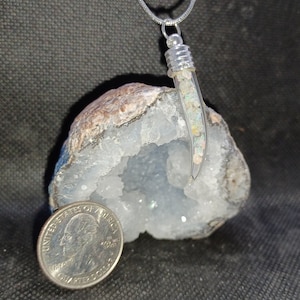 May include: A silver chain necklace with a clear glass pendant filled with small, iridescent opal pieces. The pendant is shaped like a tooth and is resting on a white geode.