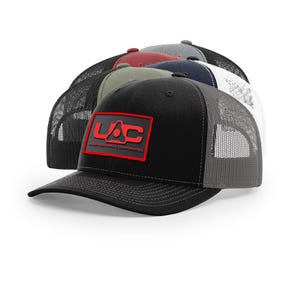 May include: A stack of trucker hats in various colors, including black, gray, red, and navy blue. Each hat features a mesh back and a front panel with a logo that reads "UAC UNION AEROSPACE CORPORATION".