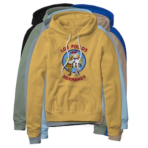 May include: A mustard yellow hooded sweatshirt featuring a graphic of two cartoon chickens inside a blue circle with the text Los Pollos Hermanos in red. The hoodie has white drawstrings and a front kangaroo pocket, layered over other hoodies.